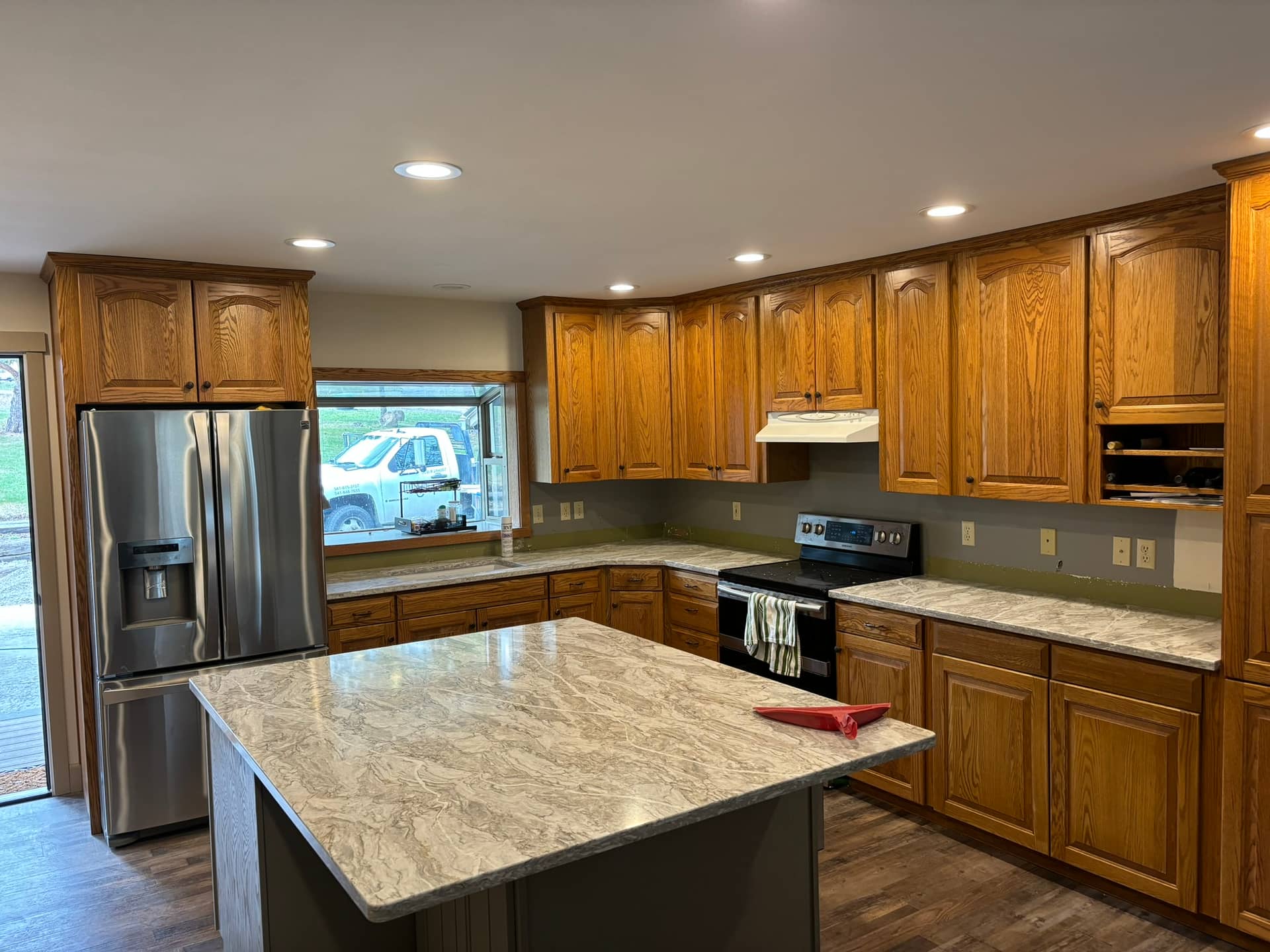 partially remodeled kitchen with stained cupboards, stainless steel appliances, and white marble counter tops with a floating island in the middle and stone back splash