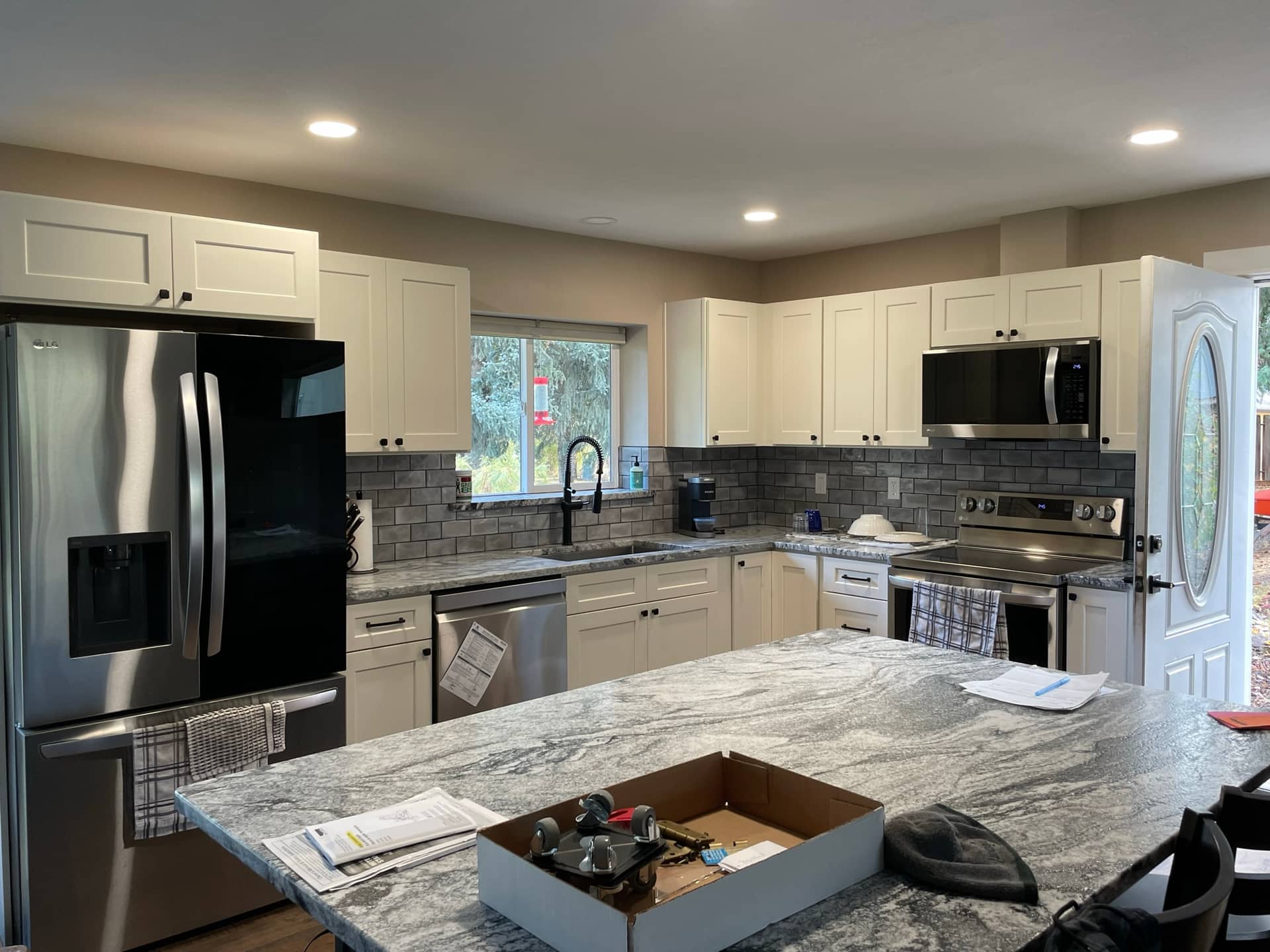 remodeled kitchen with white cupboards, stainless steel appliances, and white marble counter tops with a floating island in the middle and stone back splash